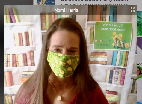 Nomi Harris, with a fake bookshelf backdrop and a pear facemask. 