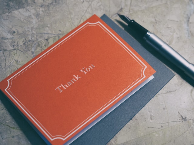 A simple post card on the table with the 'Thank you' written on it. Next to it is an ink pen.